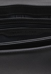 Interno di una borsa in pelle nera con texture, dotata di tasca con zip. Presenta un logo impresso e rivestimento a contrasto. Cerniere lisce.