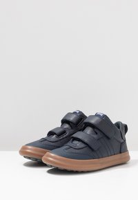 Sneakers blu navy con tomaia in pelle testurizzata e rete, con cinturini in velcro e suola in gomma marrone. Presentano un design a profilo basso.