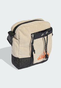 Borsa beige testurizzata con fondo nero, dotata di tasca frontale, doppie cerniere e accento logo arancione. Tracolla regolabile per il trasporto.