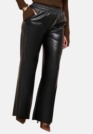 Woman wearing shiny black faux leather wide-leg pants, brown ribbed sweater, brown pointed heels, and gold bracelets on one wrist.