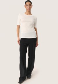 Witte, kortekorte top gecombineerd met zwarte, wijde broek. De top is aansluitend en iets doorzichtig; de broek heeft een gladde textuur en verticale lijnen.