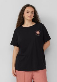 Zwarte katoenen t-shirt met opgerolde korte mouwen, uitgevoerd met een roze bloemenafbeelding en de tekst "Vul je dagen met zonneschijn."