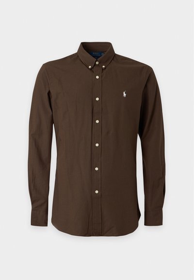 Chemise marron foncé à manches longues avec boutons, col boutonné et petit logo blanc sur le côté gauche de la poitrine.