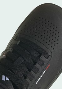 Scarpa sportiva nera con superficie testurizzata, perforazioni sulla punta e logo sul lato che recita "FREERIDER PRO." Presenta lacci neri.