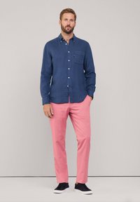 Navyblauw linnen shirt met een borstzak, gecombineerd met lichtroze broeken. Het model draagt een paar zwarte sneakers. Eenvoudig, casual ontwerp.