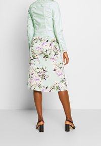 Světle modrá džínová bunda s midi sukní vzorovanou květinami. Sukně má pastelové barvy a fialové květy. Podpatky se silným podpatkem dokončují vzhled.