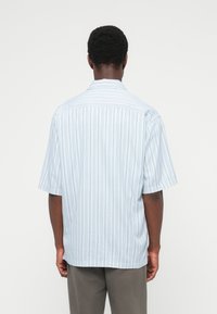 Πουκάμισο με κοντά μανίκια σε ανοιχτό γαλάζιο χρώμα με κάθετες λευκές ρίγες. Διαθέτει κλασικό γιακά και άνετη εφαρμογή, κατασκευασμένο από ελαφρύ ύφασμα.