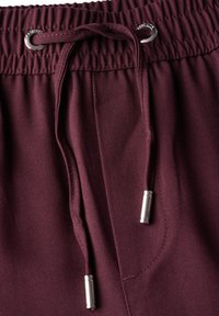 Shorts de jogging bourgogne avec taille élastique et cordon de serrage ajustable. Comprend des embouts en métal argenté et un tissu texturé.