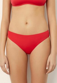 Costume da bagno rosso in tessuto liscio, con un design a taglio alto e una vita larga. Senza motivi visibili o dettagli in metallo.