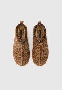 Luipaardprint pantoffels met een bruine basis. Zachte binnenvoering, elastische band en decoratieve rand. Platte rubberen zool voor comfort.