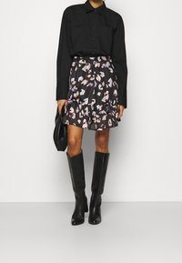 Zwarte button-up shirt gecombineerd met een gestreepte zwarte rok met roze en witte abstracte ontwerpen; kniehoge zwarte laarzen maken de look compleet.