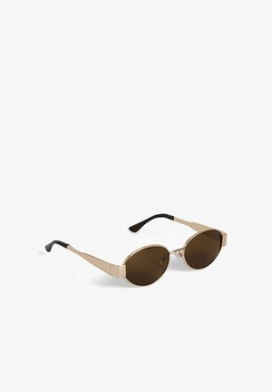 Oválne slnečné okuliare s hnedými šošovkami, zlatým kovovým rámom a čiernymi koncovkami stránic, ležiace na bielom povrchu.