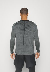 Langärmliges Sportshirt in Dunkelgrau mit strukturiertem Muster, ausgestattet mit reflektierenden Akzenten und einem schwarzen Rundhalsausschnitt.