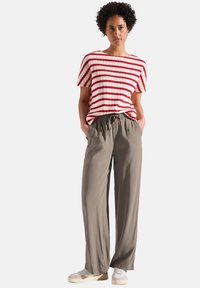 Rood-wit gestreepte gebreide top met korte mouwen, gecombineerd met losse, lichtgrijze verstelbare broek en witte sneakers.