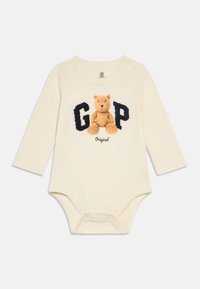 Body niemowlęce z długim rękawem w kolorze kremowym, z okrągłym dekoltem, ozdobione misiem i napisem "GAP" w granacie. Zapięcia na zatrzaski u dołu.