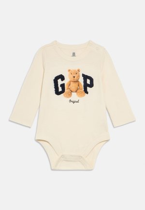 Body entero de manga larga para bebé en color crema con cuello redondo, con un osito y el texto "GAP" en azul marino. Cierres de presión en la parte inferior.