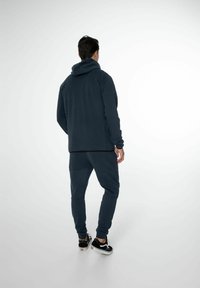 Haut de survêtement zippé bleu marine avec capuche, assorti à un pantalon fuselé. Fabriqué en tissu doux avec une texture lisse, doté de poches latérales.