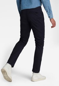 Pantaloni chinos blu navy a taglio slim, con tasche posteriori e una texture liscia. Abbinati a sneakers bianche alte e una camicia di jeans azzurro chiaro.