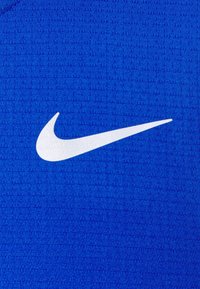 Nike sportovní látka v jasně modré barvě s texturovaným povrchem. Obsahuje výrazné bílé logo Swoosh na pravé straně.