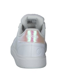 Bijela Adidas tenisica od glatke kože, s sjajnom iridescentnom potplatom i teksturiranim gumeni potplat. Ima logotip branda i oznaku unutar.