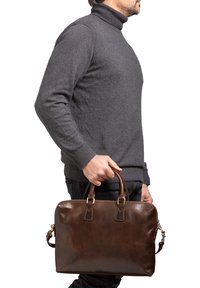 Attaché en cuir marron avec doubles poignées, texture lisse, accents en métal doré et une bandoulière amovible.