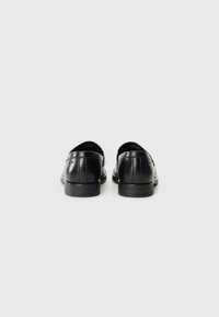 Pantofi din piele neagră cu un finisaj neted, vârf rotunjit, toc jos și detalii de cusătură subtile. Prezintă logo-ul brandului pe toc.