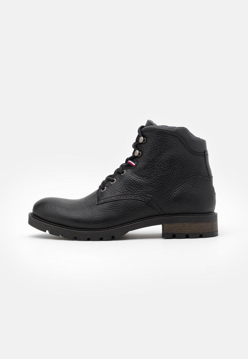 Bottine en cuir noir texturé avec lacets à l’avant, col rembourré et semelle robuste avec petit talon en bois, vue de profil sur fond blanc.