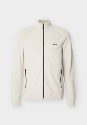 Veste blanche à fermeture éclair intégrale avec col, poignets et ourlet côtelés, dotée d'une fermeture éclair noire et de poches latérales, avec le logo "BOSS" embossé sur la poitrine.