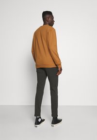 Brun crewneck sweatshirt, mørkegrå tapered bukser og sorte high-top sneakers. Glat stof, afslappet pasform, med ribbede manchetter og sømme.