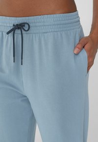 Jasnoniebieskie dresy wykonane z miękkiej tkaniny, z elastycznym paskiem w talii i sznurkiem do regulacji. Widoczne boczne kieszenie podkreślają luźny krój.