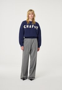 Felpa navy con la scritta "CHAPOT" in lettere crema, abbinata a pantaloni larghi grigio a righe. Finitura in tessuto liscia, vestibilità rilassata.