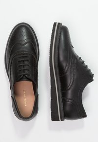 Černé kožené oxfordské boty s brogue detailem, s kulatou špičkou, šněrováním a gumovou podrážkou se šedými pruhy. Malé logo na stélce.