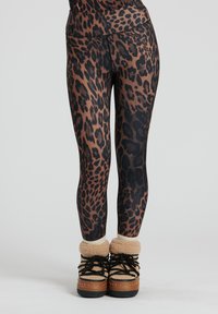Leggings con stampa leopardata e vita alta, caratterizzati da tonalità di marrone e nero, abbinati a stivali foderati in pelliccia color cammello.