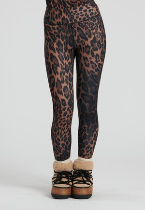 Leggings con stampa leopardata e vita alta, caratterizzati da tonalità di marrone e nero, abbinati a stivali foderati in pelliccia color cammello.