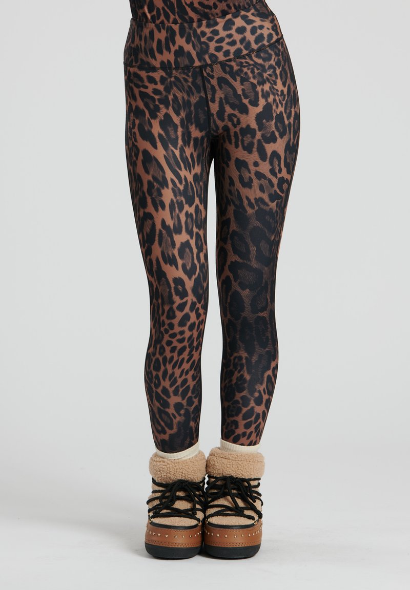 Leggings con stampa leopardata e vita alta, caratterizzati da tonalità di marrone e nero, abbinati a stivali foderati in pelliccia color cammello.