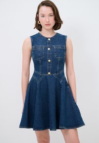 Robe sans manches en denim avec un corsage ajusté, deux poches poitrine, fermeture à boutons, jupe évasée et coutures contrastées dans une teinte bleu foncé.