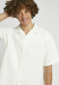 Chemise blanche à manches courtes avec une texture. Dotée d'un col classique et d'une coupe décontractée. Convient pour un usage décontracté.