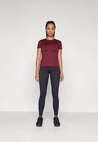 Burgundia lühikeste varrukatega sportlik topp, mida on ühendatud mustade retuusidega. Sile kangas, liibuv lõige ja ümmargune kaelus. Kandmist täiustavad mustad spordijalatsid.