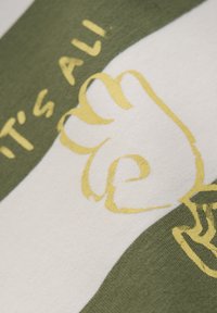 Vihreä ja valkoinen raidallinen kangas, jolla on teksturoitu tunne. Siinä on keltaista graafista tekstiä ja nyrkin kuva. Rennon tyylinen, puuvillamateriaali.