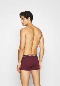 Boxers bordeaux avec une ceinture élastique noire et brandée. Portés par un mannequin masculin vu de dos, montrant un tissu lisse et une coupe ajustée.