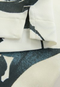 Fabric top featuring a cream base with large blue and black abstract floral patterns, smooth texture, folded collar, and neat stitching details.