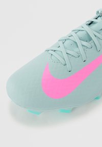 Light blue soccer cleat with a textured upper, featuring a prominent pink Nike logo and light blue accents on the sole and laces.