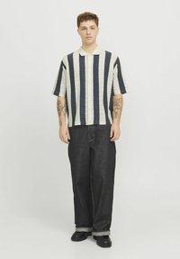 Camicia a maniche corte con colletto, a righe zigzag blu navy e crema; abbinata a jeans neri in denim larghi e scarpe nere con suola spessa.