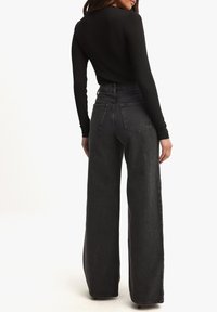 Jeans negros de cintura alta con piernas anchas, confeccionados en tela de mezclilla. Presentan bolsillos traseros clásicos y detalles de costura sutiles.