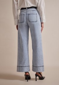 Light blue wide-leg jeans made of denim, featuring back pockets and a stitched hem. Paired with black high-heeled shoes.