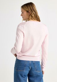 Lyserød striktrøje med lange ærmer og ribbet kant, kombineret med blå, højtaljede denimjeans. Glat tekstur og enkelt design.