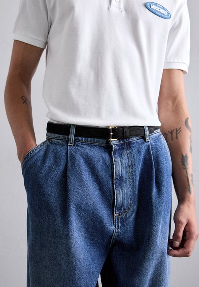 Valge polo särk Moschino logoga, must nahkne vöö ja laiad, helehallid teksapüksid, millel on esiosad ja sile tekstuur.