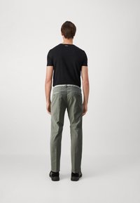 T-shirt noir à manches courtes, pantalon vert olive et chaussures noires. Le pantalon est équipé de poches zippées et d'un léger revers à l'ourlet.