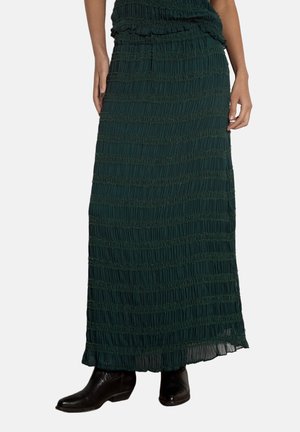 Gonna lunga maxi verde scuro con trama, indossata con stivaletti neri, mostrata su una persona dalla vita ai piedi su uno sfondo neutro.