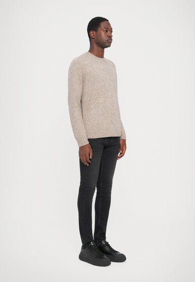 Pullover in lana beige chiaro con scollatura rotonda, indossato con jeans skinny neri e sneakers nere, creando un look casual.